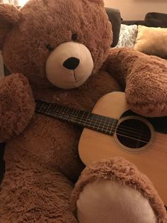 a brown teddy bear sitting on top of a couch holding a guitar