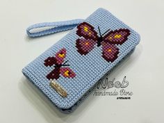 a cross - stitch wallet with a butterfly design on the front and side, sitting on a white surface