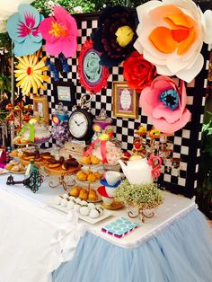 a table topped with lots of food next to a wall covered in pictures and paper flowers