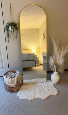 a mirror sitting on top of a floor next to a vase filled with dry grass