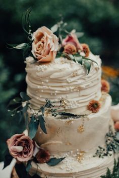 a wedding cake with flowers and greenery on top