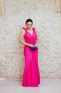 a woman in a bright pink dress standing next to a wall with a flower on it