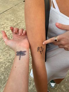 two women with matching tattoos on their arms pointing at each other's wrists