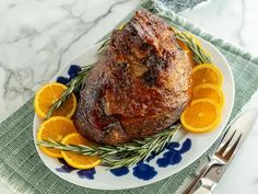 a plate with meat, oranges and rosemary garnish on it next to silverware