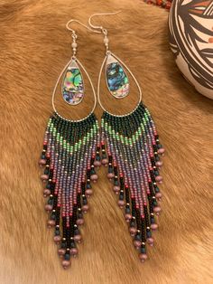 "Long fringe hanging from teardrop frames with an abalone style shell charm hanging in the middle. There is a combination of fire polished beads accenting the ends of each fringe and a mother of pearl at the top with sterling silver French hooks. They measure 6 1/2\" from hook to the longest fringe." Bohemian Teardrop Jewelry With Dangling Beads, Bohemian Iridescent Beaded Jewelry, Beaded Fringe Teardrop Earrings As Gift, Bohemian Silver Tassel Earrings With Beaded Fringe, Bohemian Long Drop Chandelier Earrings With Dangling Beads, Long Drop Chandelier Earrings With Dangling Beads, Unique Teardrop Jewelry With Dangling Beads, Silver Jewelry With Beaded Fringe For Festivals, Teardrop Beaded Jewelry For Festivals