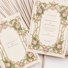 two wedding cards with roses on them sitting next to each other in front of fans