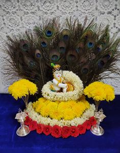 an arrangement of flowers and peacock feathers on a blue table cloth with a statue in the center