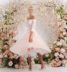 a woman in a pink dress posing for the camera with flowers around her and an archway behind her