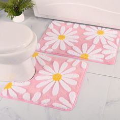 two pink and white bathroom rugs with daisies on them next to a toilet