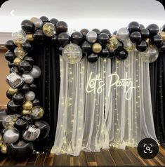 black and gold balloons are on display in front of a curtained backdrop that says let's party