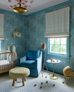 a baby's room decorated in blue and pink with a crib, rocking chair, lamp, table and window