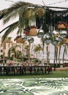 an outdoor dining area with palm trees and hanging lights over the tables, surrounded by greenery