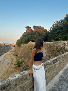 a woman leaning against a stone wall with trees in the background