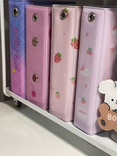 an assortment of pink, blue, and purple binders with a teddy bear on them