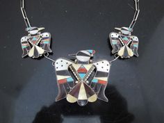 Incredibly fine handcrafted Zuni necklace by artisans Bobby and Corraine Shack.  sterling link chain necklace with 3 thunderbird pendants with multi-gemstone inlay including coral, mother of pearl, turquoise, and onyx. Each pendant is accented by sterling silver beads and roping. Two smallest pendants measures 1 3/8" x 1 1/2". Largest pendant measures 2 3/8" x 2 1/4". Total length 19". Weighs 61 grams. Engraved signature at back of main pendant.  Other pieces by this artist in this design may be available. 10738-70d Trio Necklace, Link Chain Necklace, Small Pendant, Chain Link Necklace, Sterling Silver Bead, Sterling Silber, Silver Beads, Link Chain, Mother Of Pearl