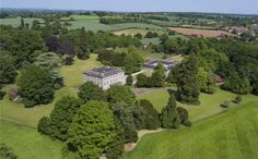 an aerial view of a large white house surrounded by green fields and wooded area with lots of trees