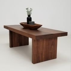 a wooden table with a bowl on it and vases in the middle, against a white background