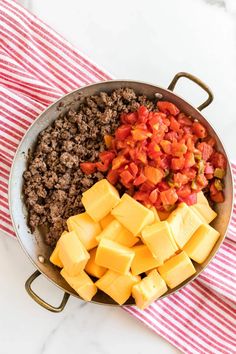 cheese, tomatoes and ground beef in a pan on a red and white striped towel