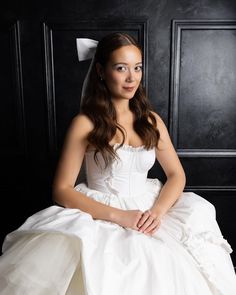 a woman in a white wedding dress sitting on a black chair with her hand on her knee