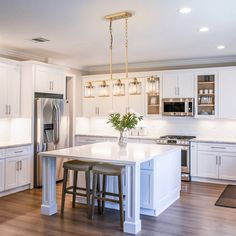 a kitchen with white cabinets and an island in the middle is lit by two pendant lights