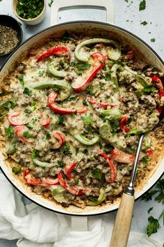 a skillet filled with meat and vegetables on top of a white cloth next to some seasonings