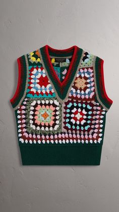 a green sweater vest with multicolored flowers on the front and back, hanging from a wall