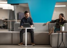 two people sitting on couches in an office setting, one using a laptop computer