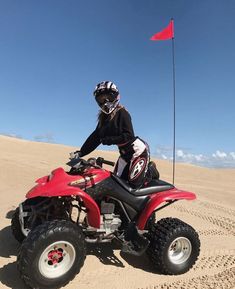 a man riding on the back of a red four - wheeler in the sand dunes