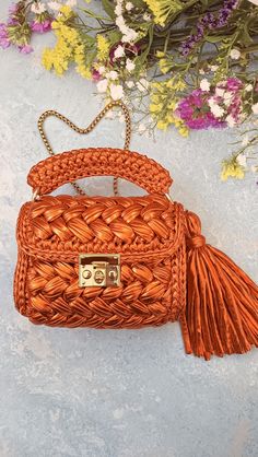 an orange woven purse sitting on top of a table next to purple and yellow flowers