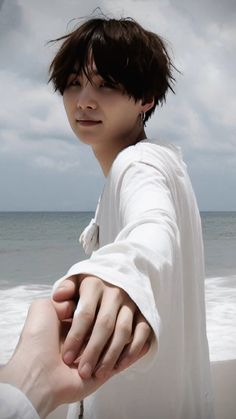 a young man holding the hand of another person on a beach with waves in the background