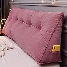 a pink pillow sitting on top of a bed next to a night stand with lights