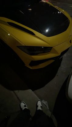 a person standing next to a yellow sports car in the dark with their feet on the ground