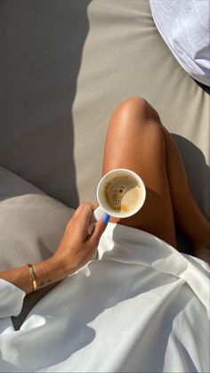 a woman laying in bed holding a cup of coffee