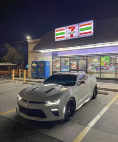 a silver sports car parked in front of a gas station at night with its lights on