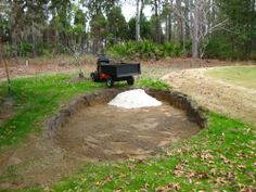 a truck parked in the middle of a dirt hole with trees and grass around it