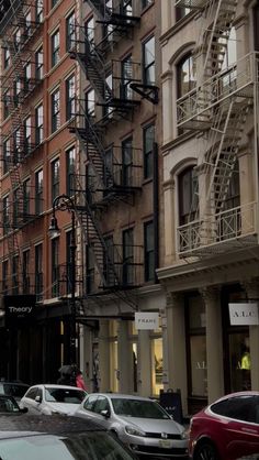 several cars parked on the street in front of tall buildings with fire escapes and staircases