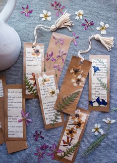 four bookmarks with flowers on them sitting next to a teapot and some paper tags