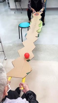 an older man is playing with a ball on a long piece of cardboard that has been cut into the shape of a road