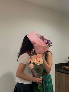 two women hugging each other with flowers in front of their faces and one holding a pink paper bag over her head