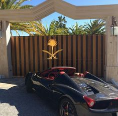 a black sports car is parked in front of a gated driveway with palm trees