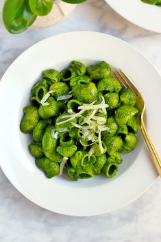 a white bowl filled with green pasta and sprouts on top of a table