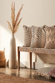 a wooden bench sitting next to a white vase filled with dry grass on top of a hard wood floor