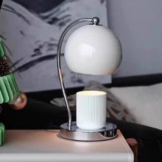 a white lamp sitting on top of a table next to a green vase and pine cone