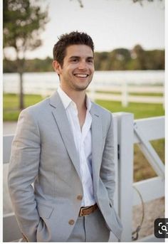 a man standing in front of a white fence wearing a gray suit and brown tie