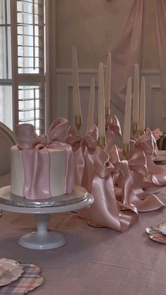 there are many candles on the table with pink ribbons around it and one cake is white