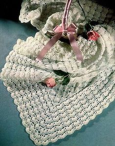 a crocheted white blanket with pink ribbon and flowers on it, next to a basket