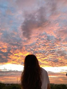 a woman standing on top of a lush green field under a colorful sky at sunset