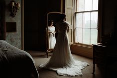 a woman standing in front of a mirror wearing a wedding dress and looking at herself in the mirror