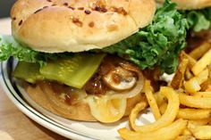 a hamburger with mushrooms, lettuce and pickles next to french fries on a plate