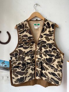 a brown and black camouflage print vest hanging on a white wall next to a horseshoe